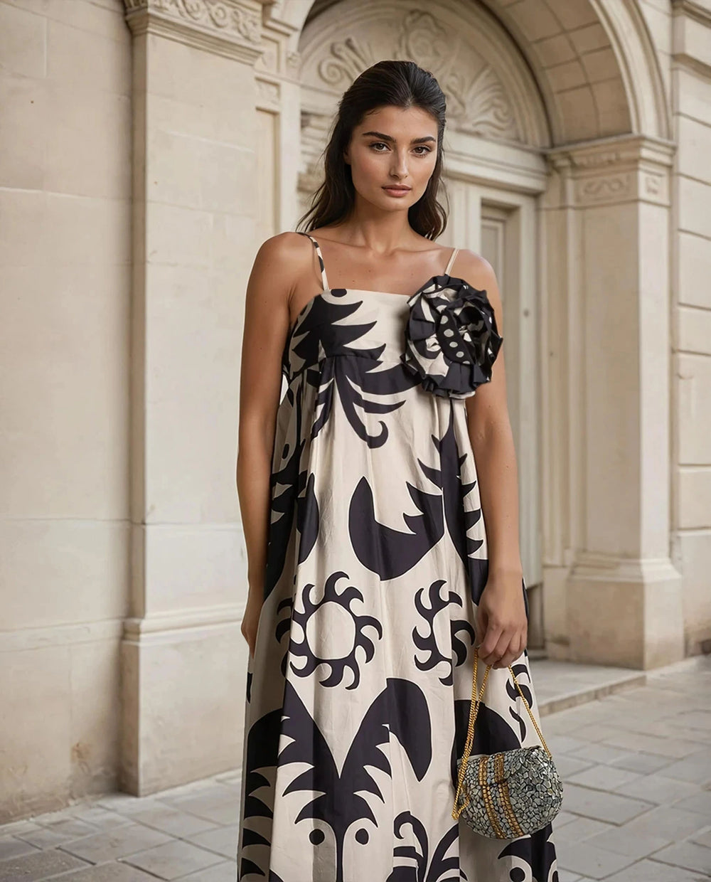Elegant maxi dress with black abstract pattern and removable flower detail, styled with a beaded mini bag
