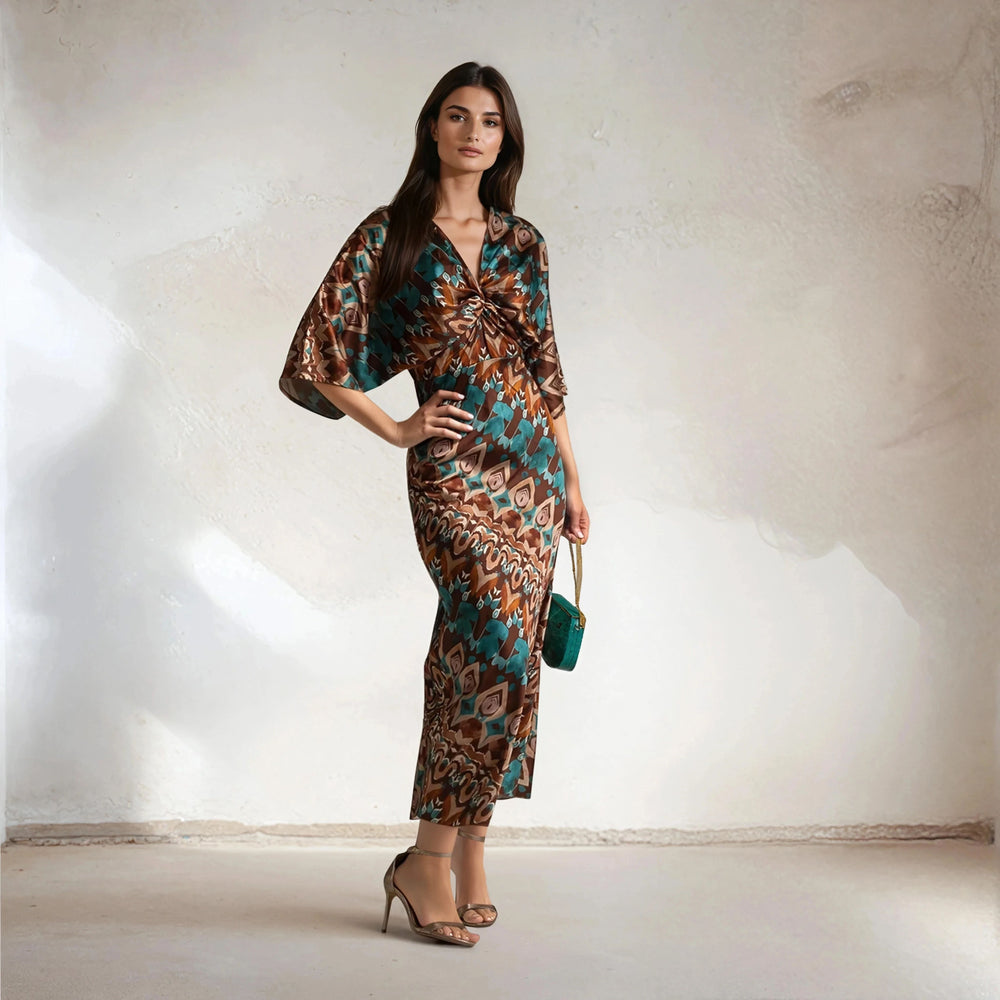 Model posing in satin Toscana dress with V-neck, teal and rust diamond print, and heels