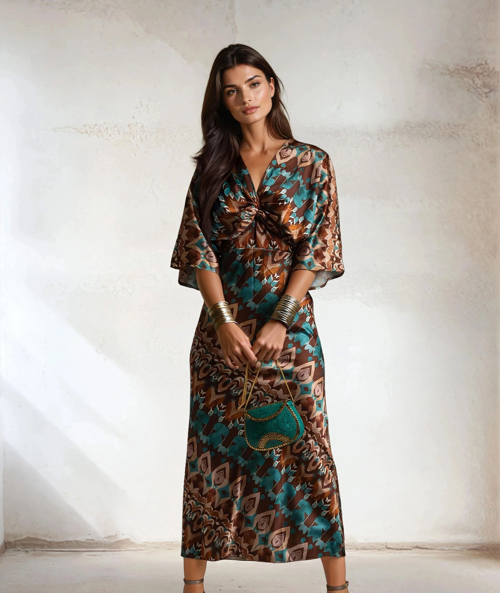 Front view of model in Toscana satin dress with geometric print holding green beaded purse