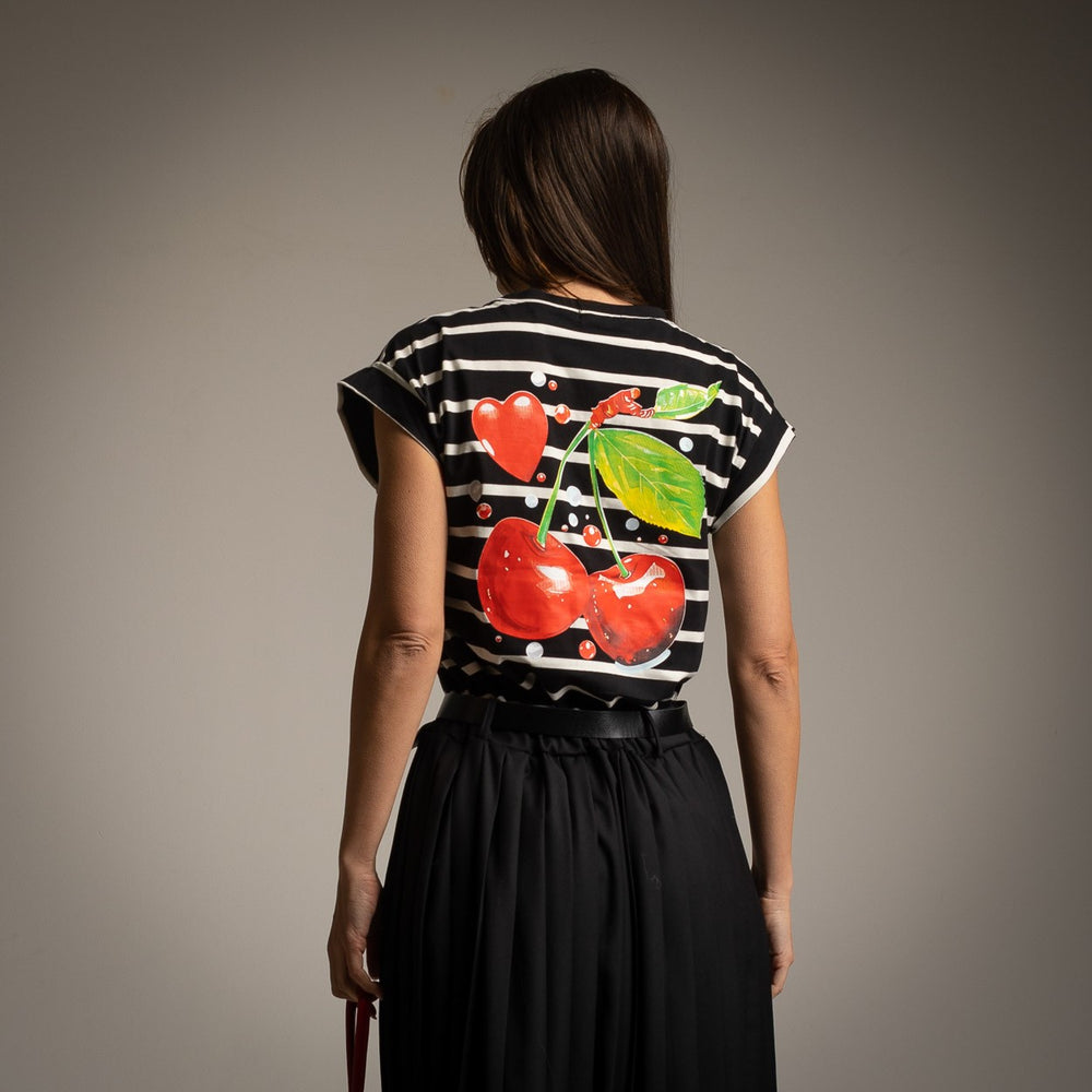Back view of a black striped T-shirt with colorful cherry and heart print, styled with a black pleated midi skirt, black base version.