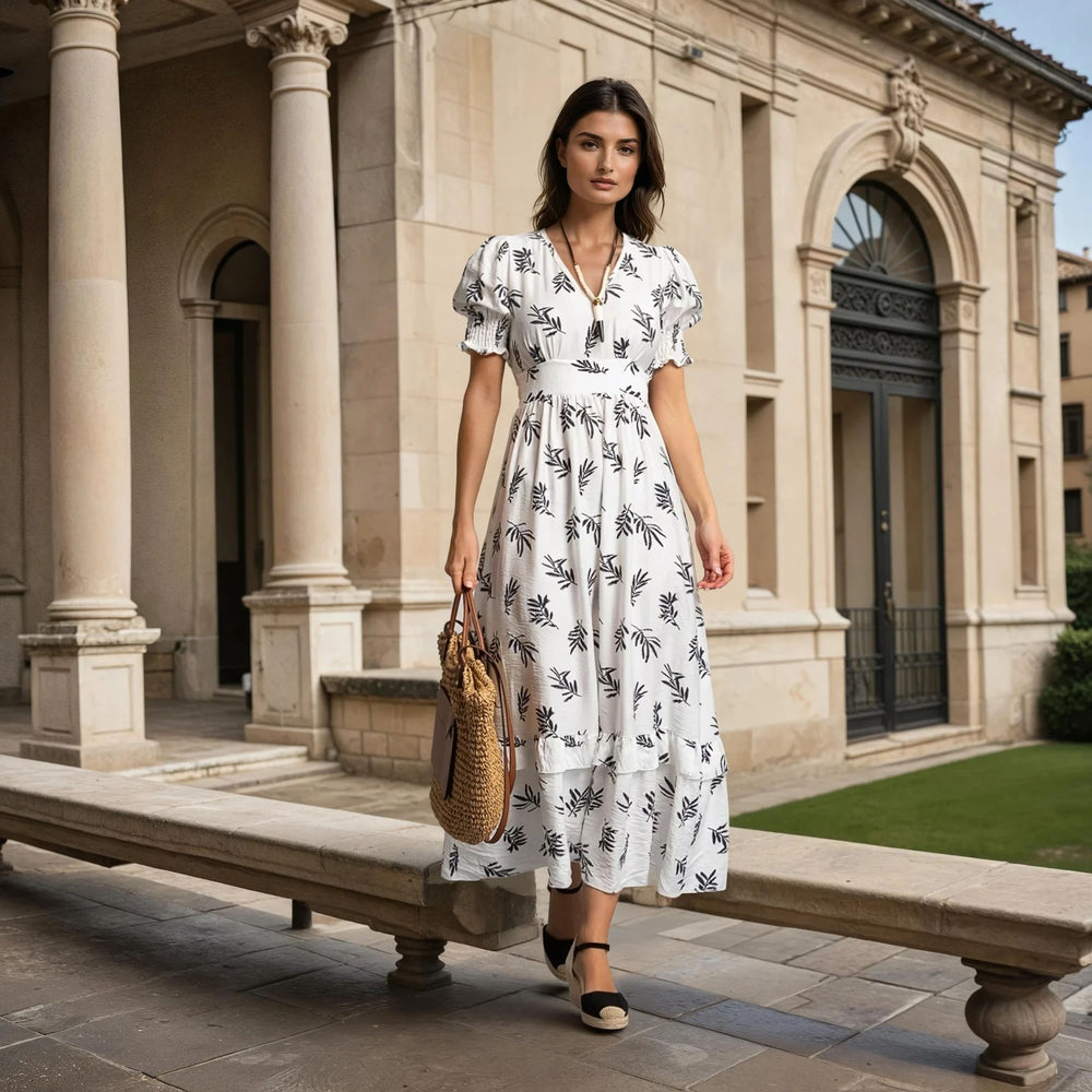 Stylish white midi one-size summer dress with leaf pattern, worn by a woman in front of a historic building, carrying a big straw bag.