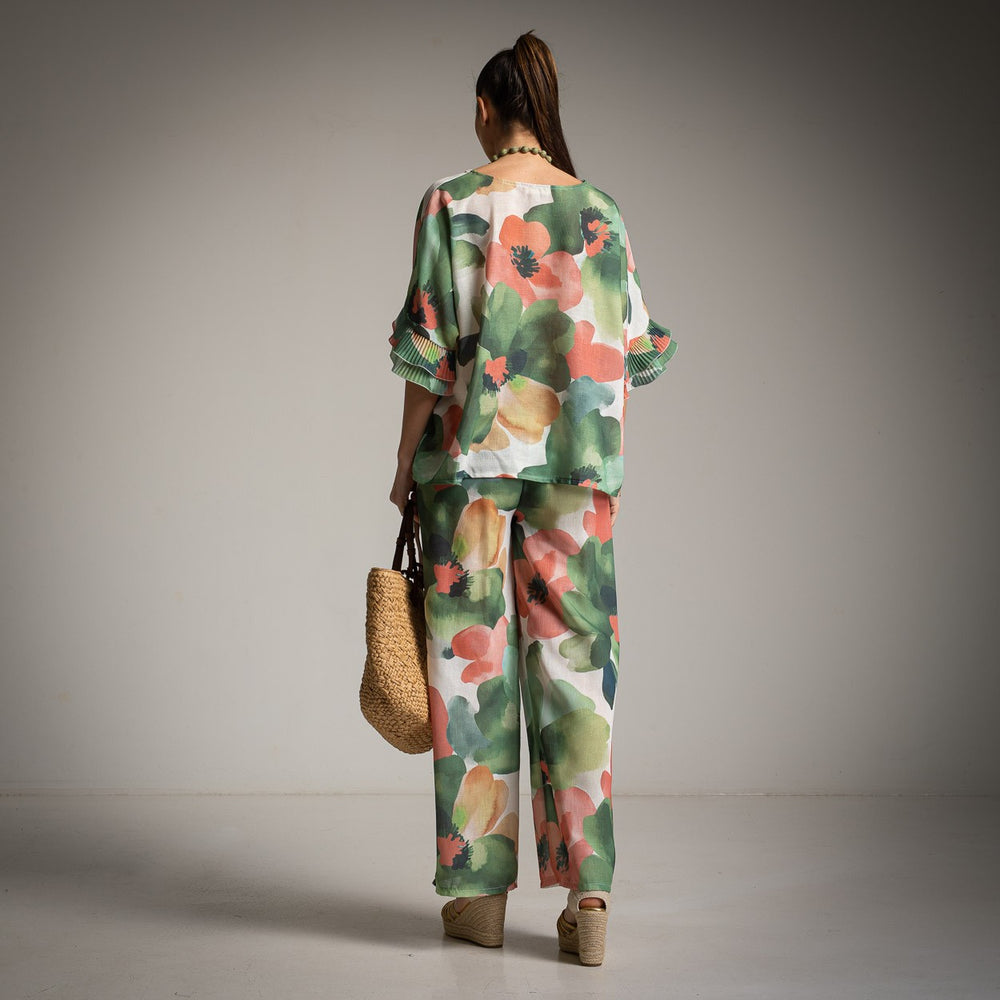 Back view of green floral pants and shirt set with ruffled sleeves and straw bag