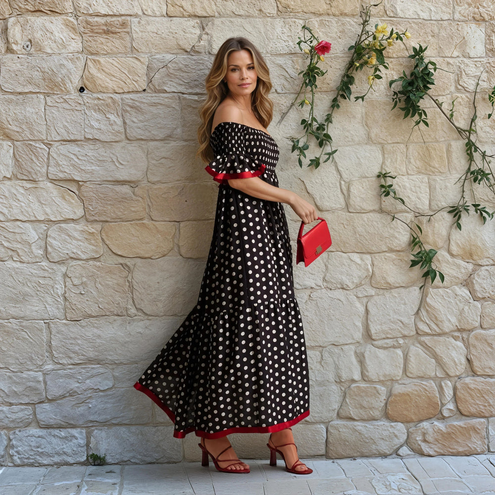 Woman in voluminous ruffle-sleeve maxi dress standing near a stone wall