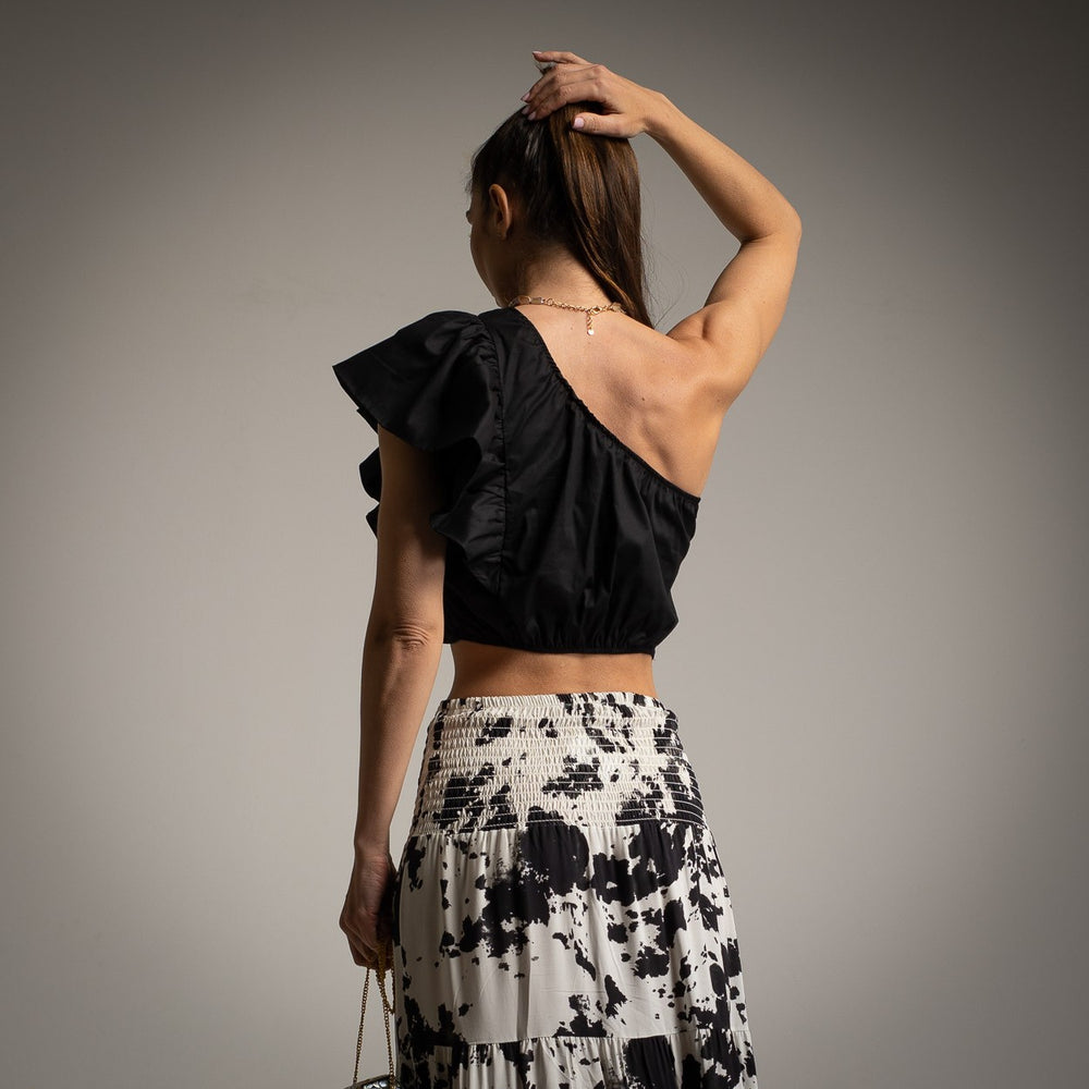 Back view of woman wearing black one shoulder crop top with ruffle and printed maxi skirt