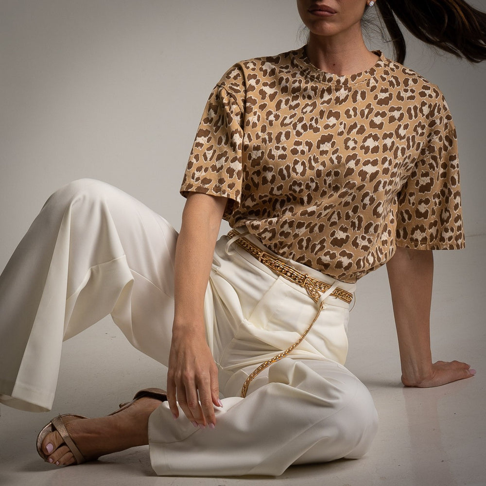 Close-up of leopard print cotton shirt tucked into white pants with gold chain belt