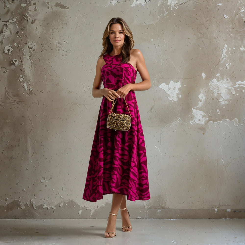 Woman wearing a bright pink sleeveless midi dress with dark magenta abstract print, holding a gold embellished handbag.