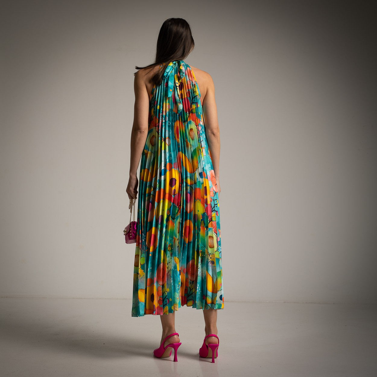 Back view of MARIΓIOÚ pleated satin halter midi dress in turquoise with halter tie and flowing pleated silhouette