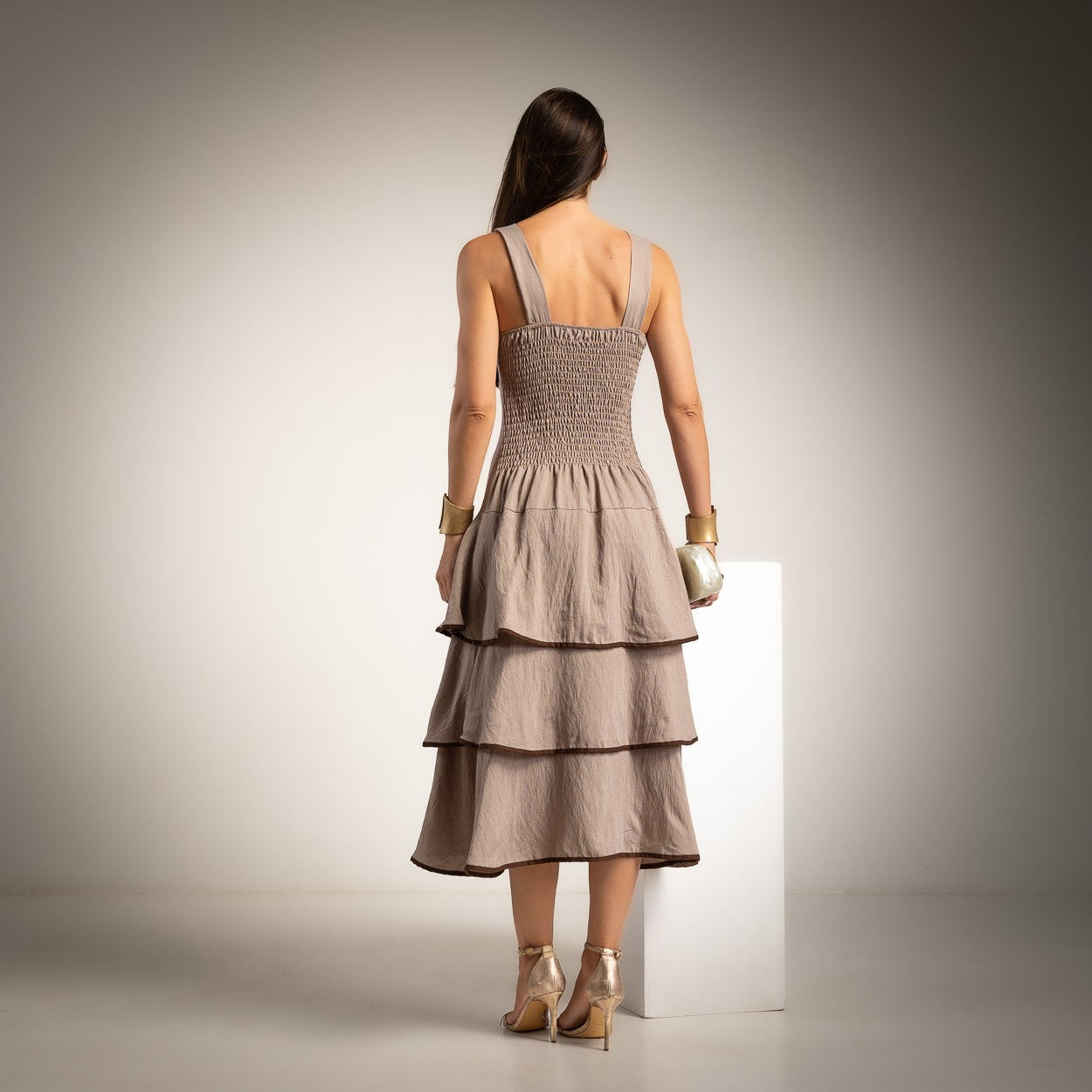 Back view of a taupe tiered midi dress featuring an elasticated back and layered ruffle skirt