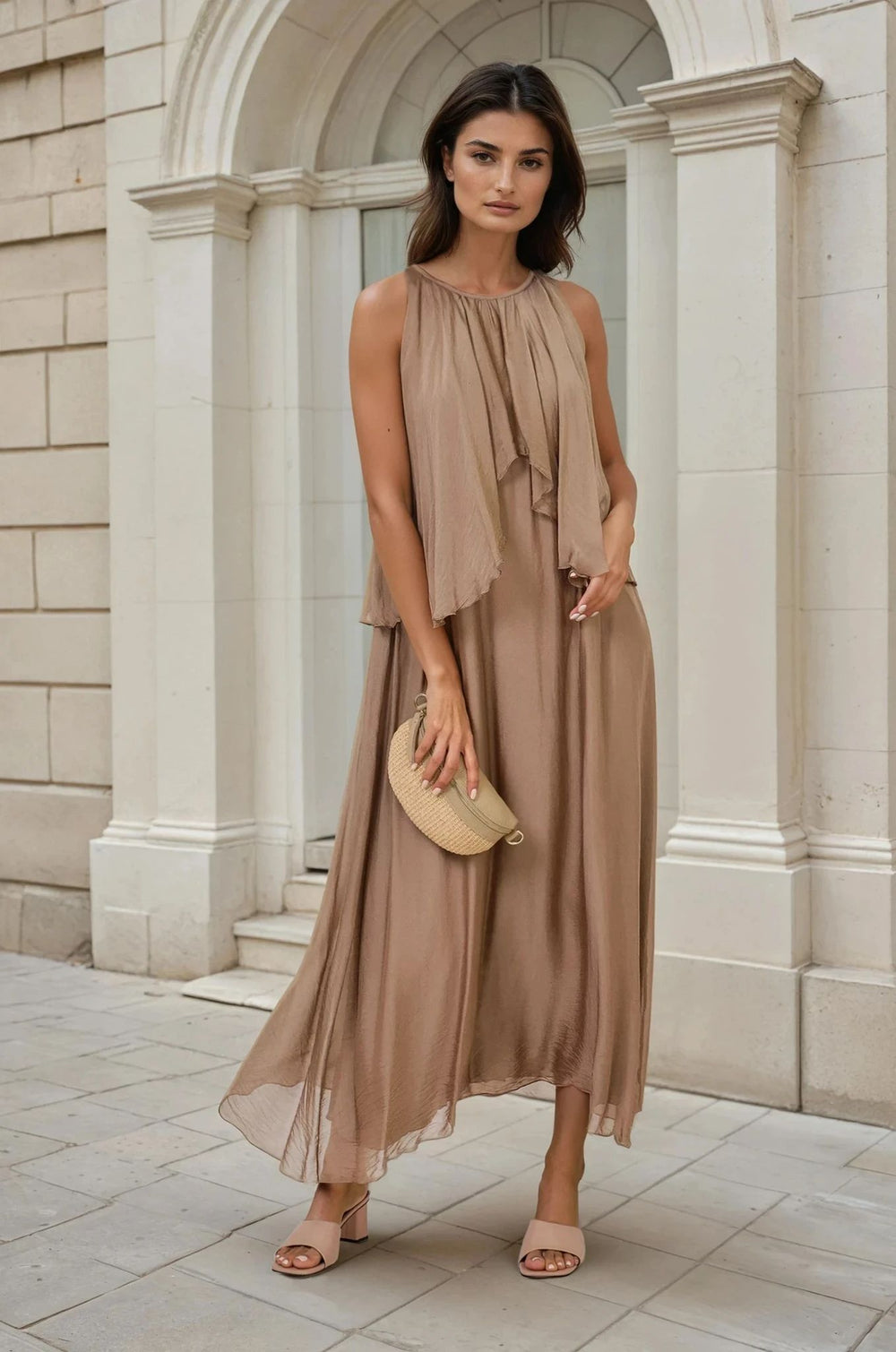 Flowy taupe long midi one size oversize dress with ruffles, worn by a woman in front of a historcial building, holding a small bag