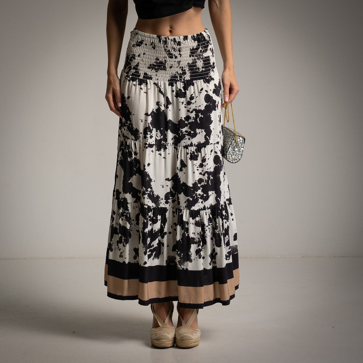 Close-up front view of maxi skirt with black abstract print and beige hemline.