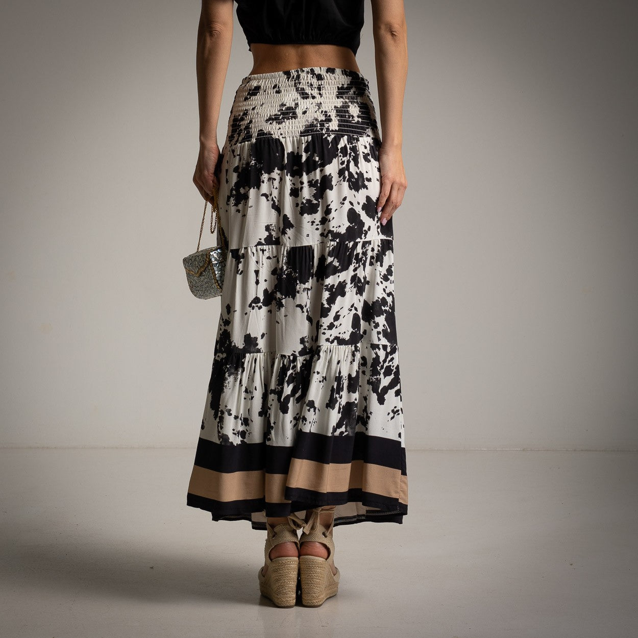 Back view of long viscose skirt in black and beige animal pattern, featuring wide smocked waistband.