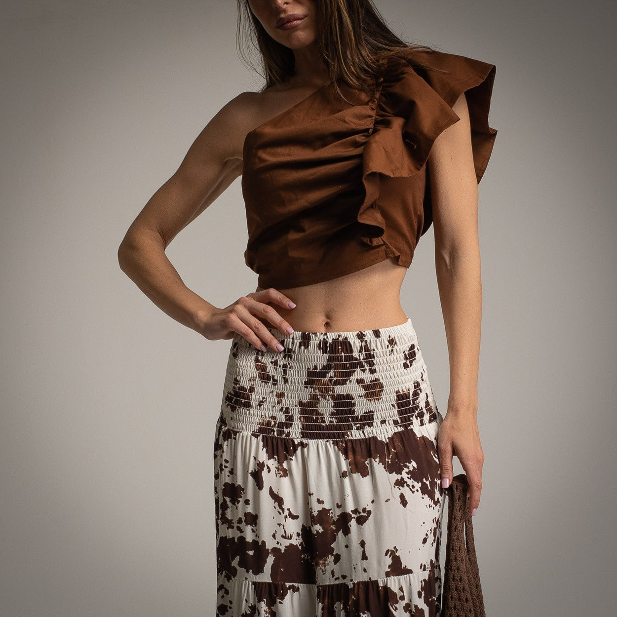 Close-up front view of brown ruffled one shoulder crop top paired with smocked waist maxi skirt