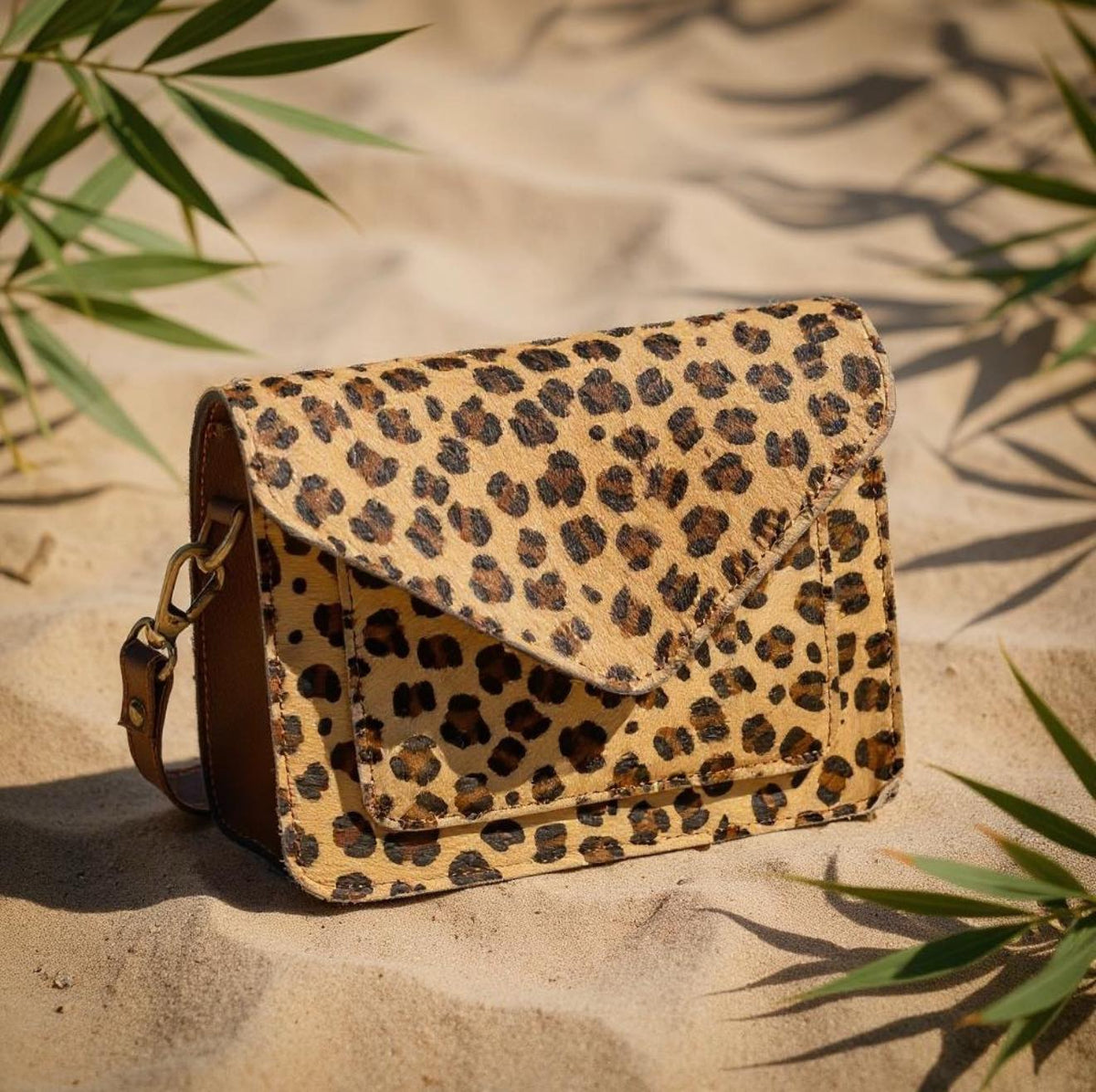 Cheetah pattern leather crossbody bag styled on sand with natural elements