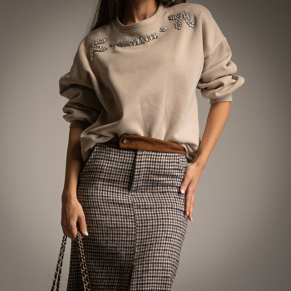 Close-up of beige embellished sweatshirt with oversized rhinestone details