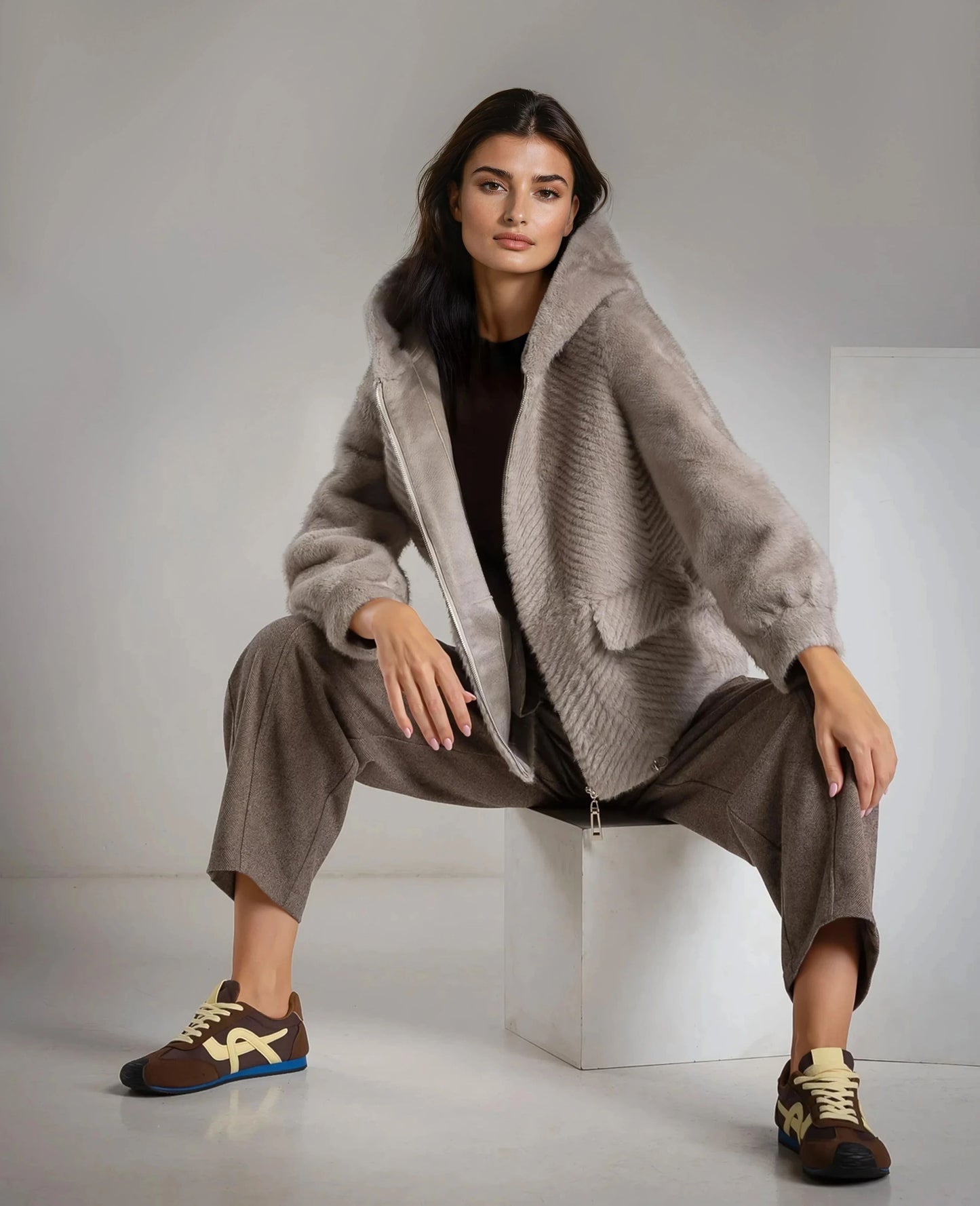 Model wearing MARIΓIOÚ faux fur hooded jacket in neutral tones, styled with tailored brown trousers.