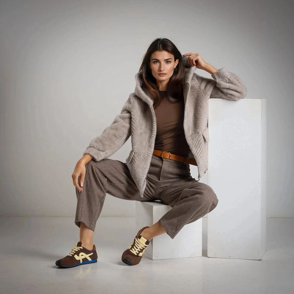 Front view of MARIΓIOÚ faux fur hooded jacket in taupe, styled with brown trousers.