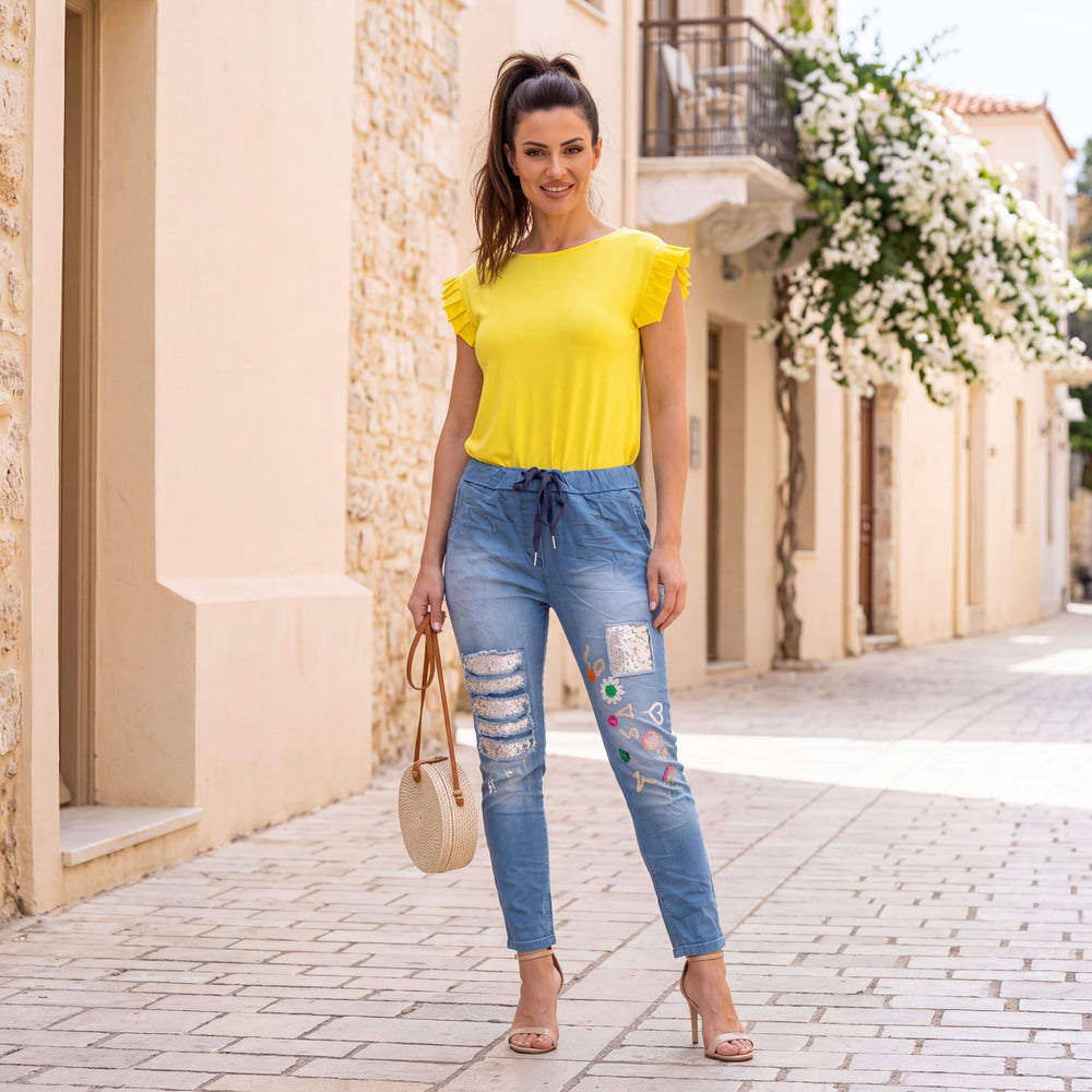 Woman wearing the Amalfi Ruffle Sleeve Top in Lemon Yellow styled outdoors with casual summer fashion.