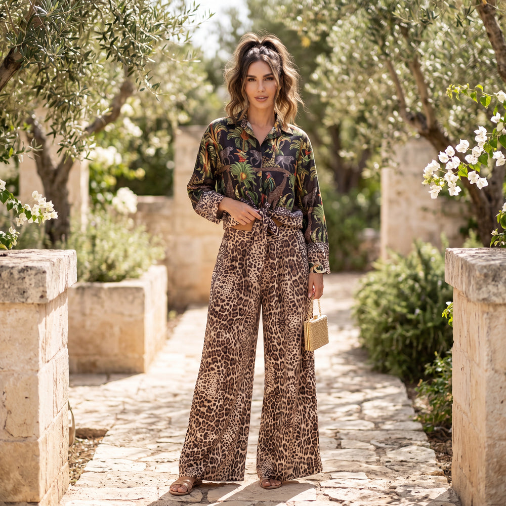 Woman wearing classic black safari print two-piece set with tropical shirt and leopard print trousers in a Mediterranean garden