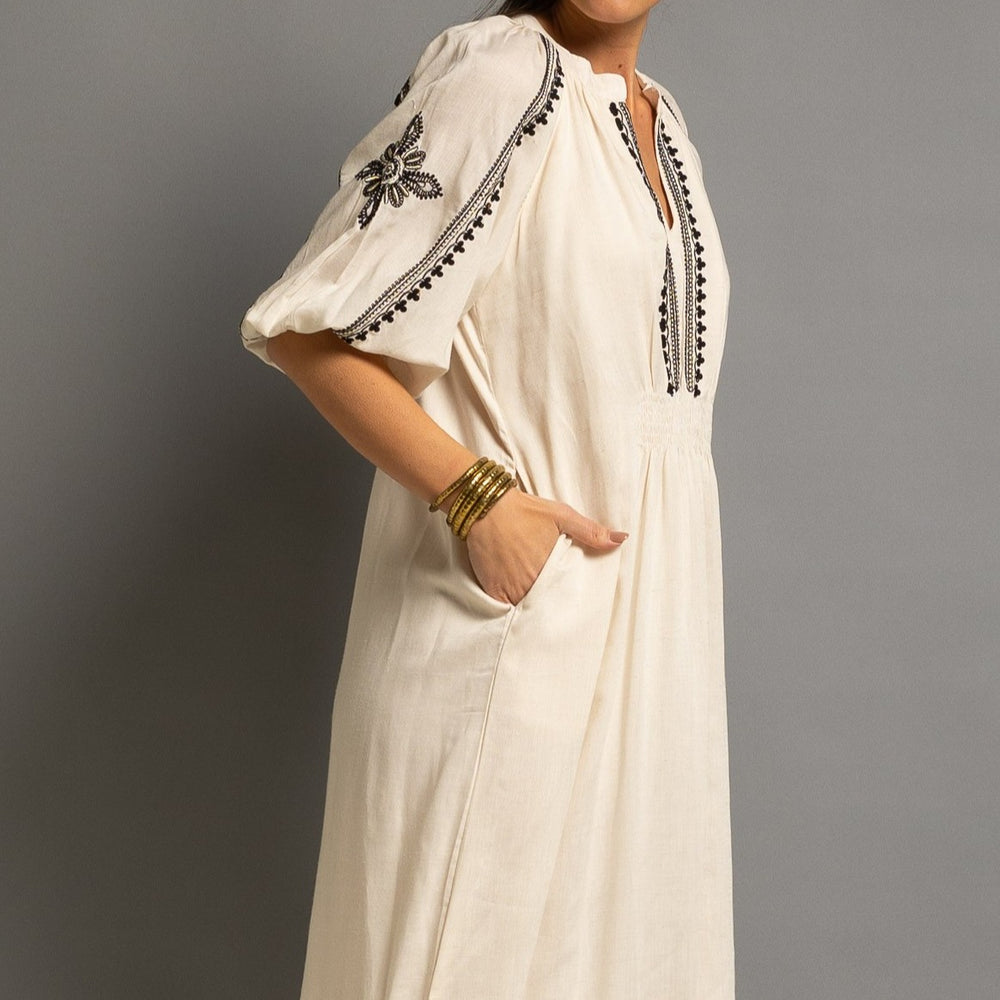 Close-up of embroidered neckline, balloon sleeve and side pocket on an elegant ivory midi dress.