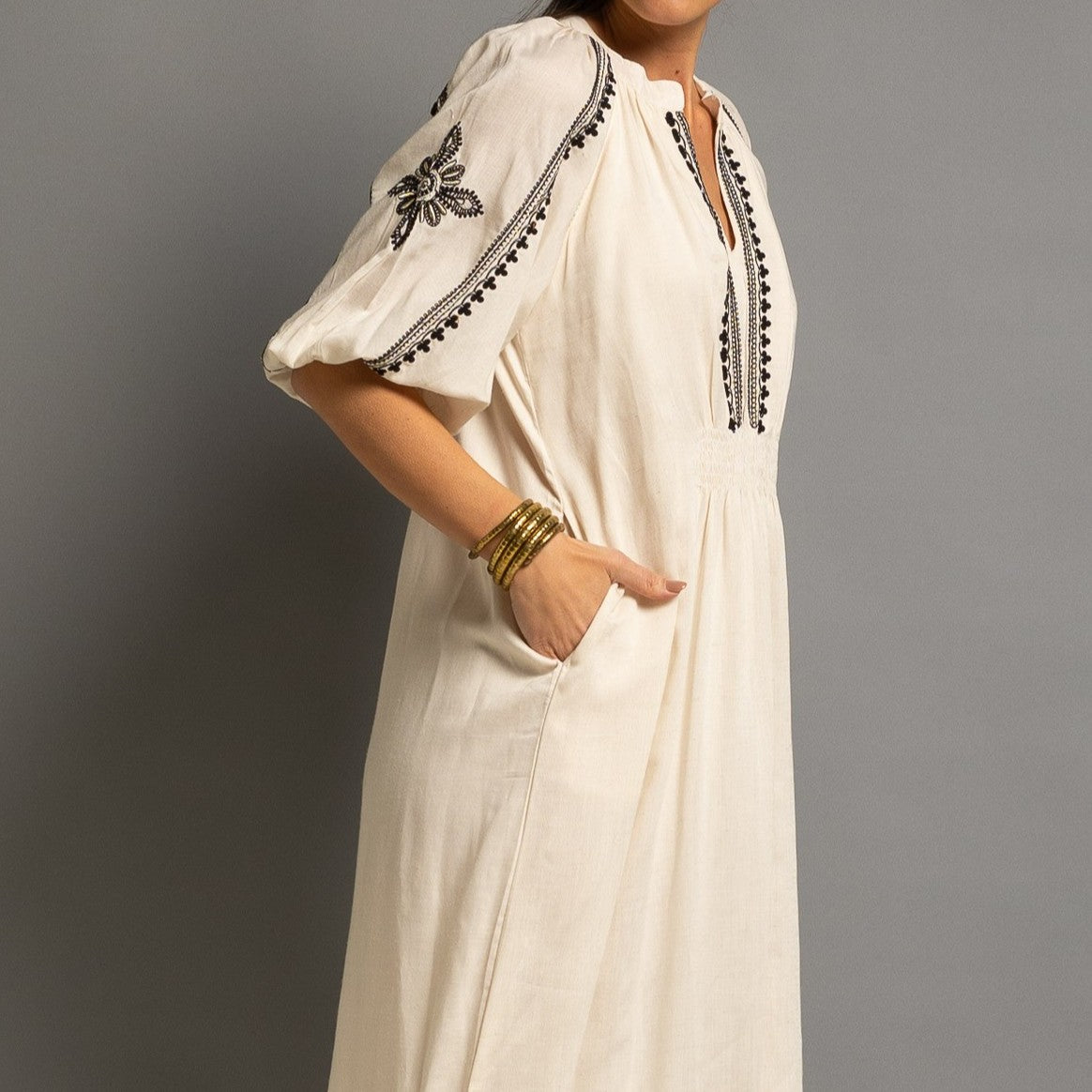 Close-up of embroidered neckline, balloon sleeve and side pocket on an elegant ivory midi dress.