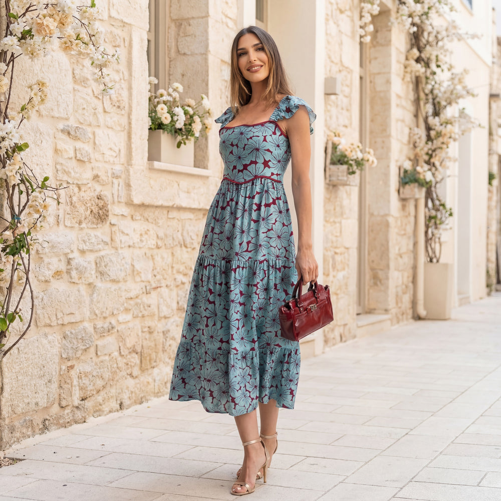 MARIΓIOÚ floral midi dress with volant straps in dusty blue, styled outdoors with red handbag in a Mediterranean setting