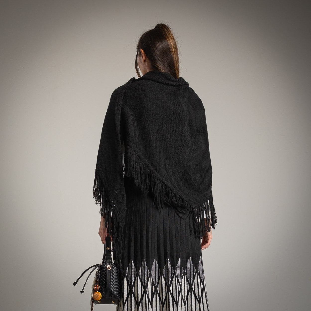 Black fringed knit shawl worn over pleated skirt – back view