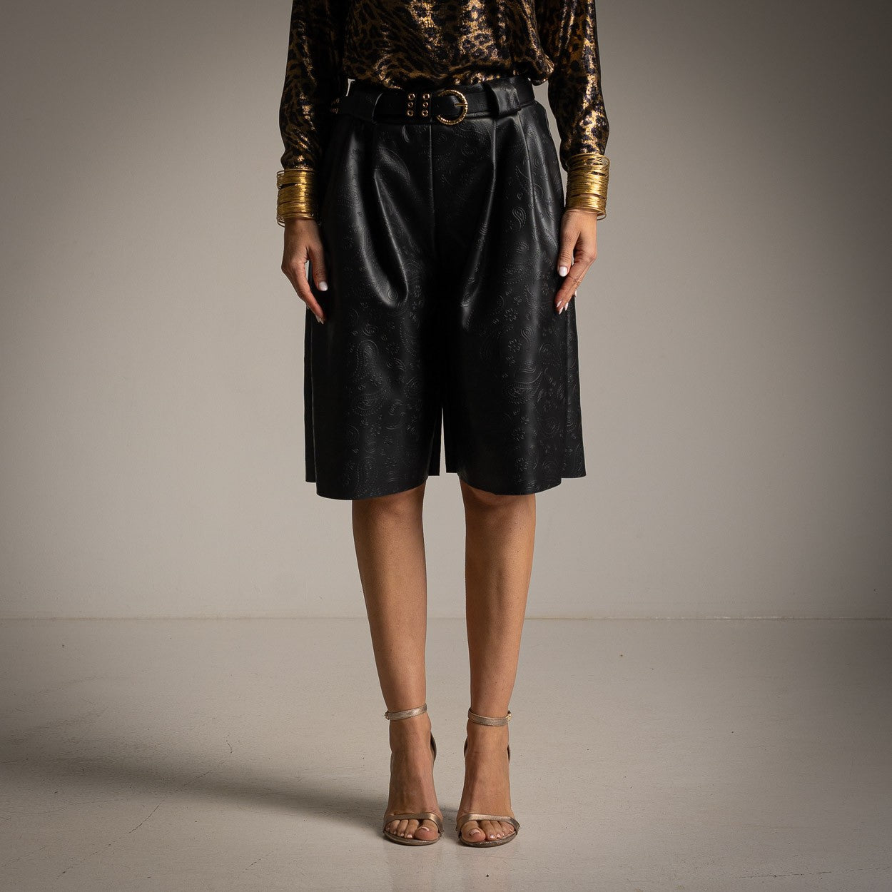Front view of high-waisted faux leather Bermuda shorts with embossed paisley pattern and matching belt.
