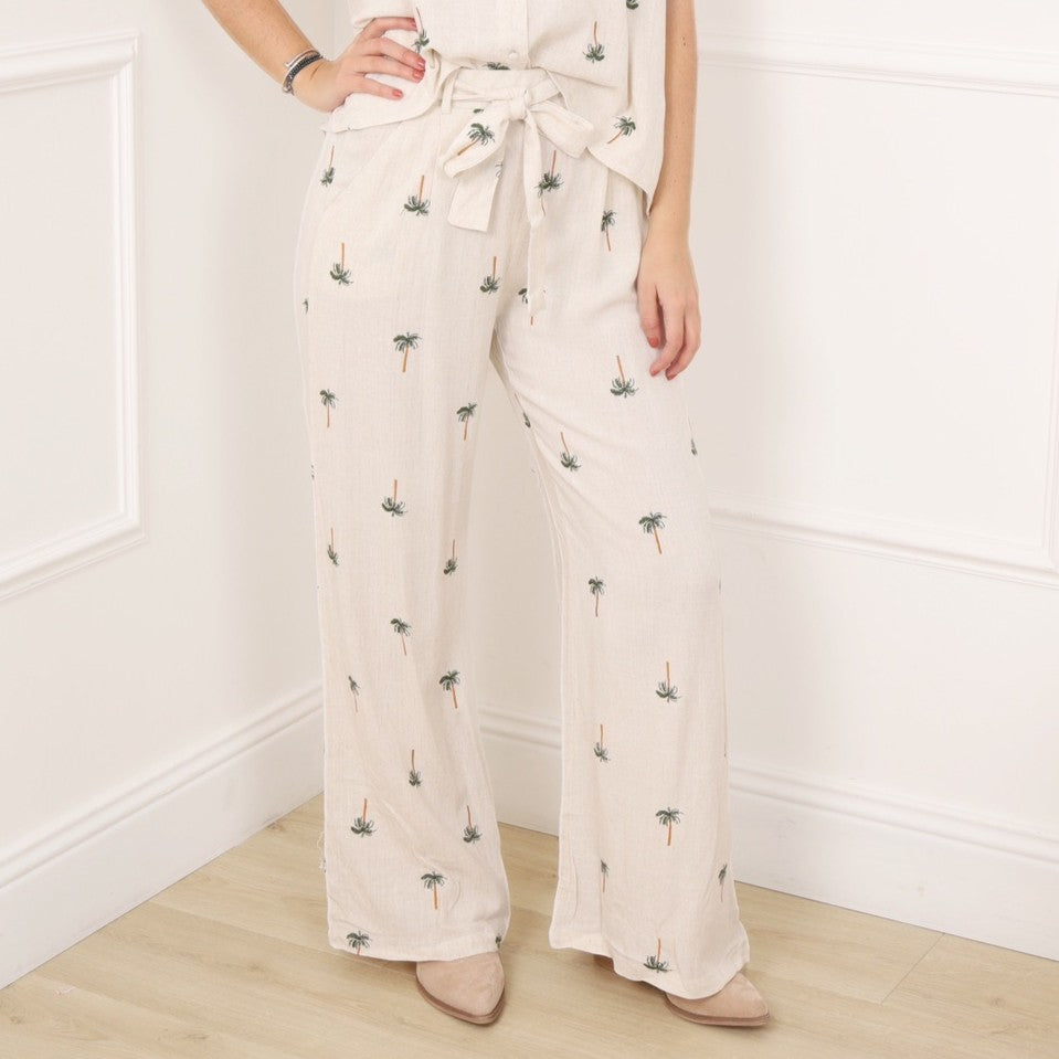 Close-up view of beige palm print wide leg pants with tie belt and relaxed fit