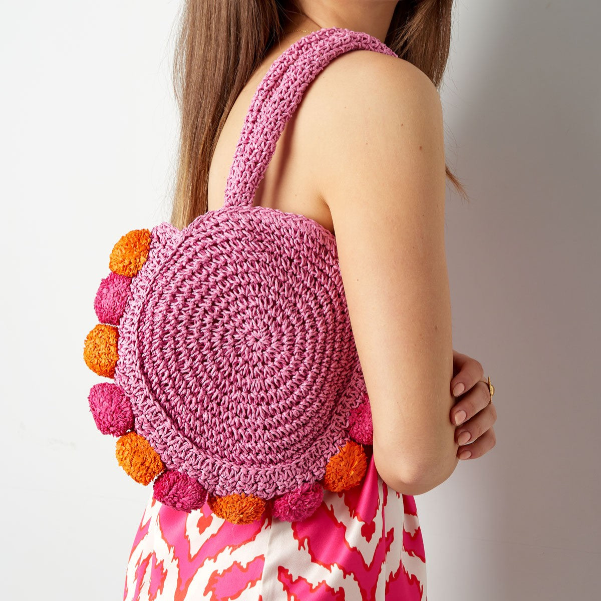 Pink Orchid Pom Pom Beach Bag worn over the shoulder showcasing its round woven design