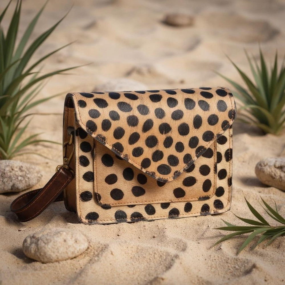 Spotted leather crossbody bag styled on sand with natural details