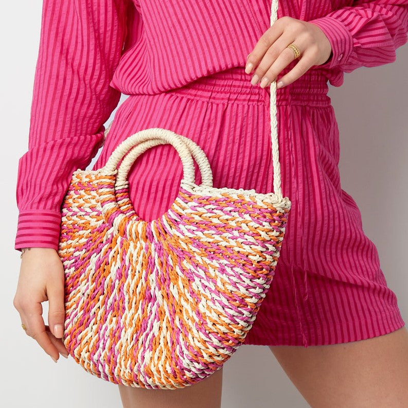 Woman carrying the Sunset Woven Beach Bag in Orchid Sunset styled with a vibrant summer outfit